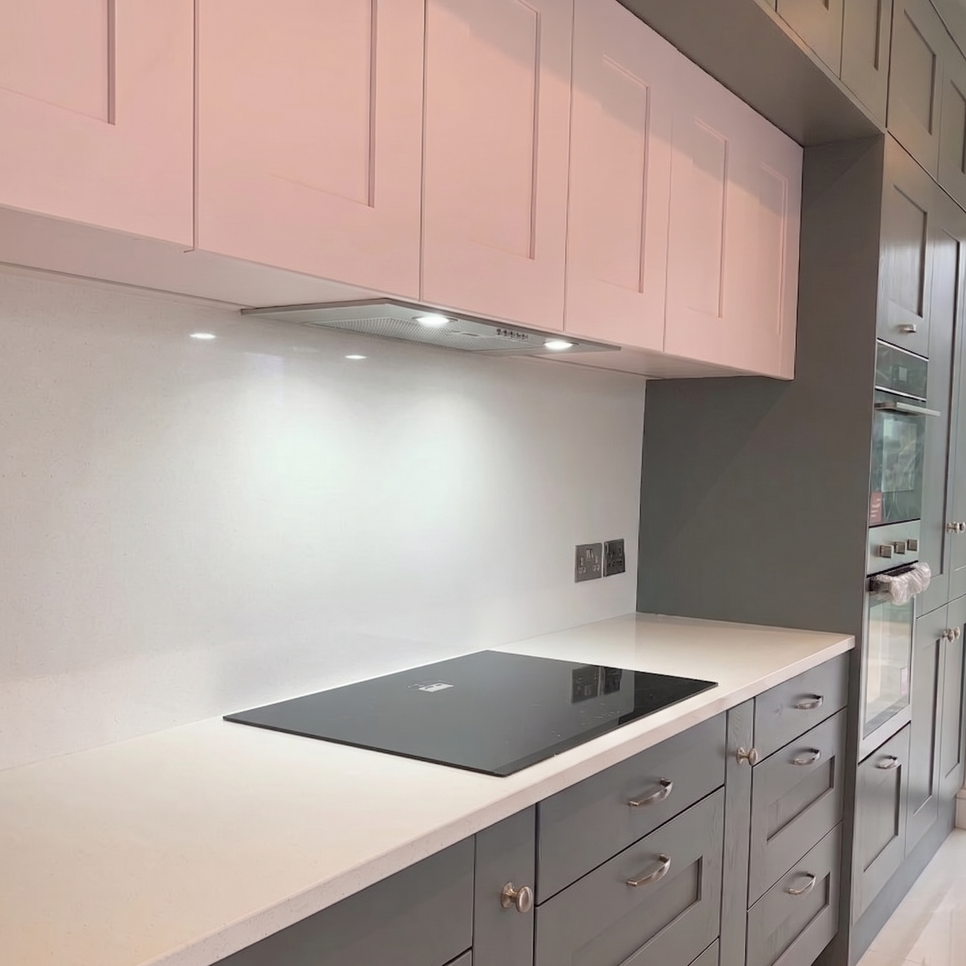 Under-cabinet view of a 54cm built-in extractor fan illuminating a white quartz countertop and black induction hob