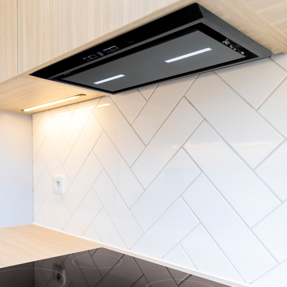 Luxair 54cm black glass canopy cooker hood with integrated LED strip lighting, installed under wood cabinets with a white herringbone tile backsplash.