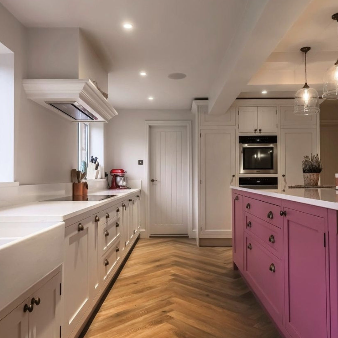 Luxair 86cm canopy stainless steel cooker hood installed in a modern white kitchen with pink island and wood chevron flooring.
