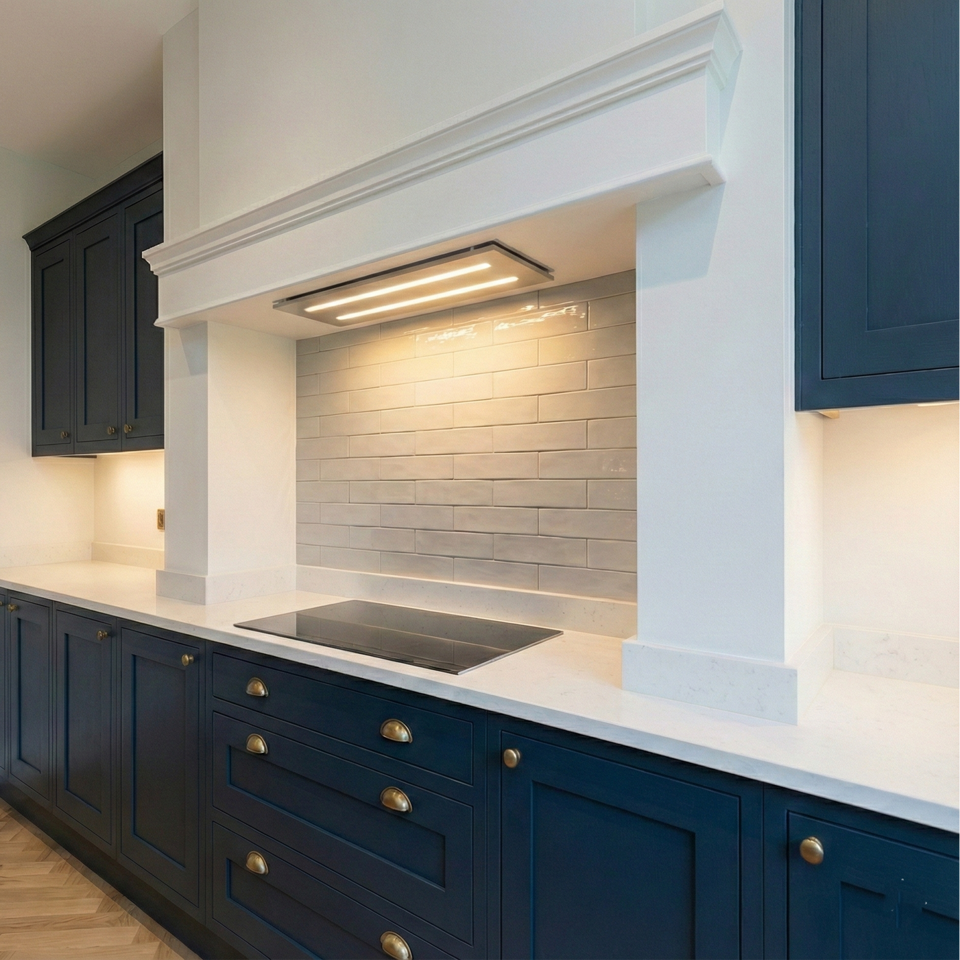 Navy blue shaker kitchen cabinets with brass handles featuring a 800mm stainless steel slimline canopy cooker hood with warm LED lighting built into a white chimney breast.