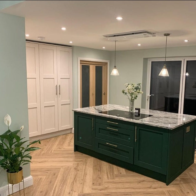 Luxair 800mm white slimline ceiling cooker hood installed over a dark forest green kitchen island with marble worktop and chevron wood flooring.