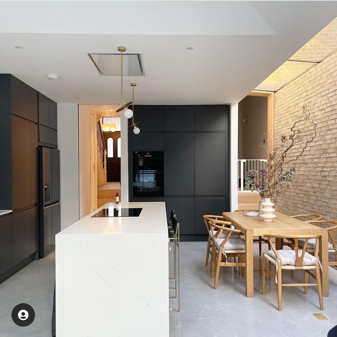 Celux White Cooker Hood Installed In A Sleek, Modern kitchen with black cabinets, white island, and wooden dining table.