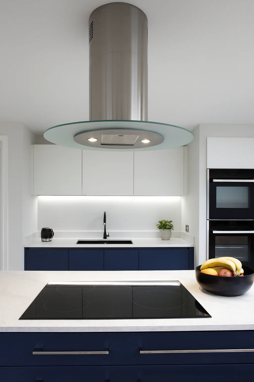 Oval island cooker hood installed within a modern white and blue minimalistic kitchen