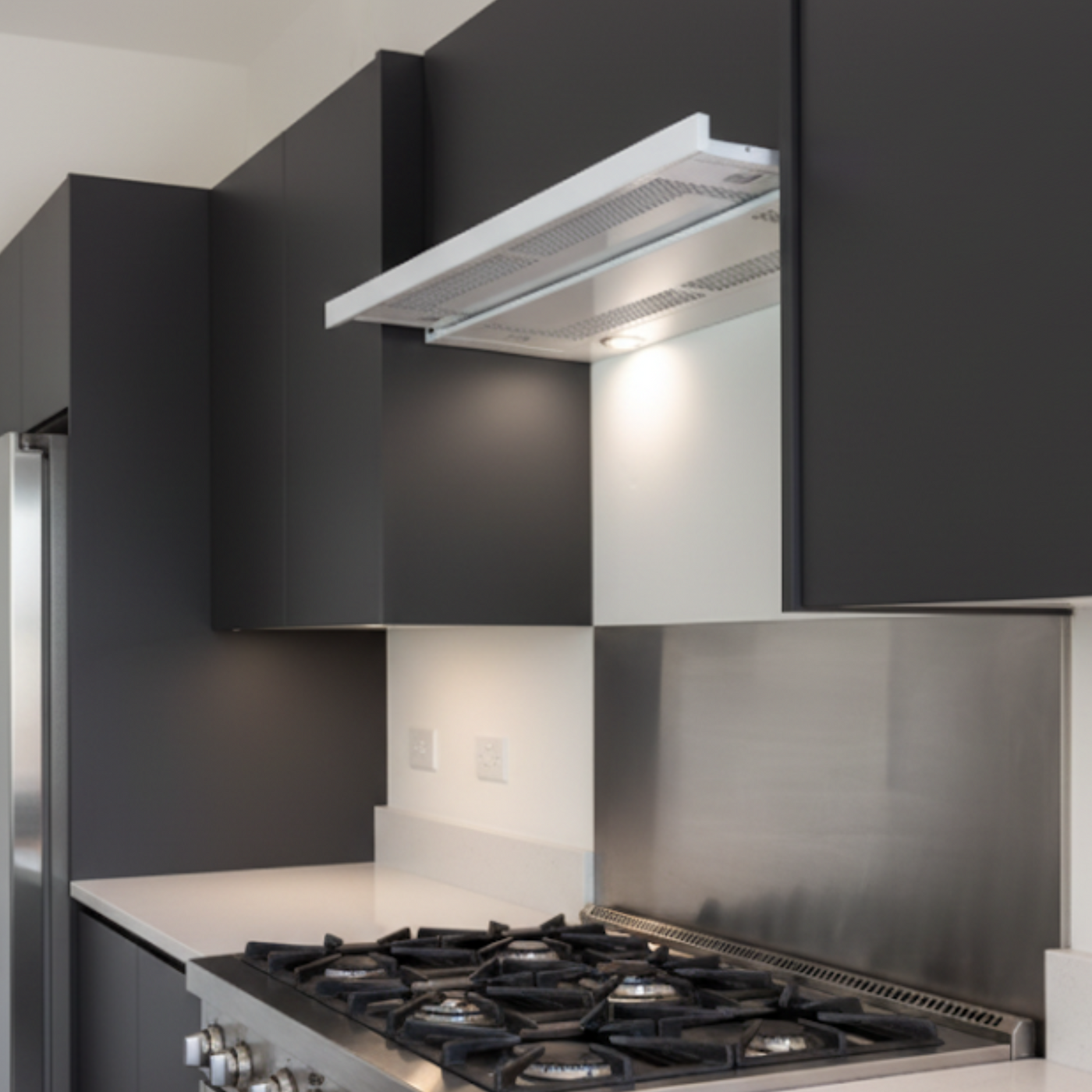 White Telescopic Cooker Hood Within A Modern kitchen With Gas Hob And Stainless Steel Splashback